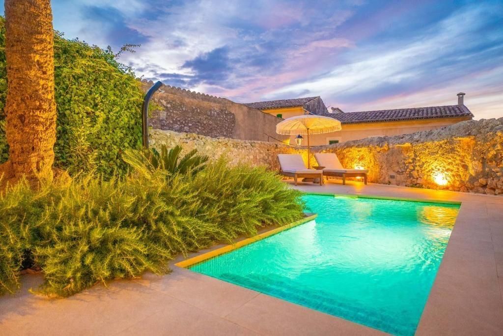 Piscina al atardecer, agua turquesa, dos tumbonas, paredes de piedra, vegetación exuberante e iluminación ambiental cálida.