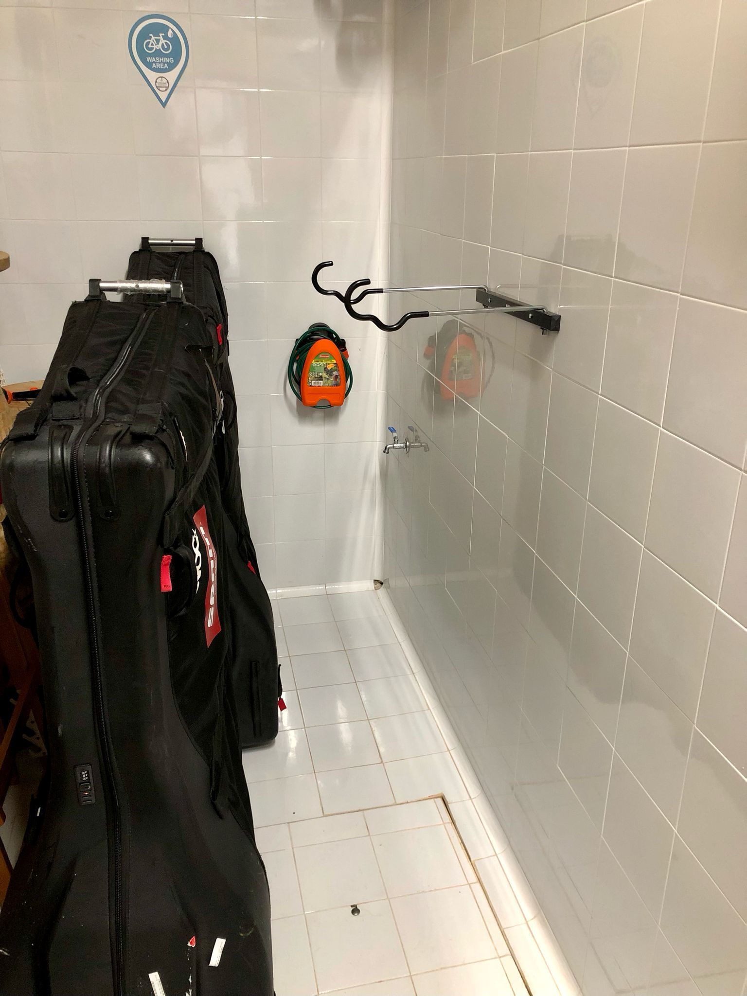 Maletas negras y un casco contra una pared de azulejos, con un portabicicletas.