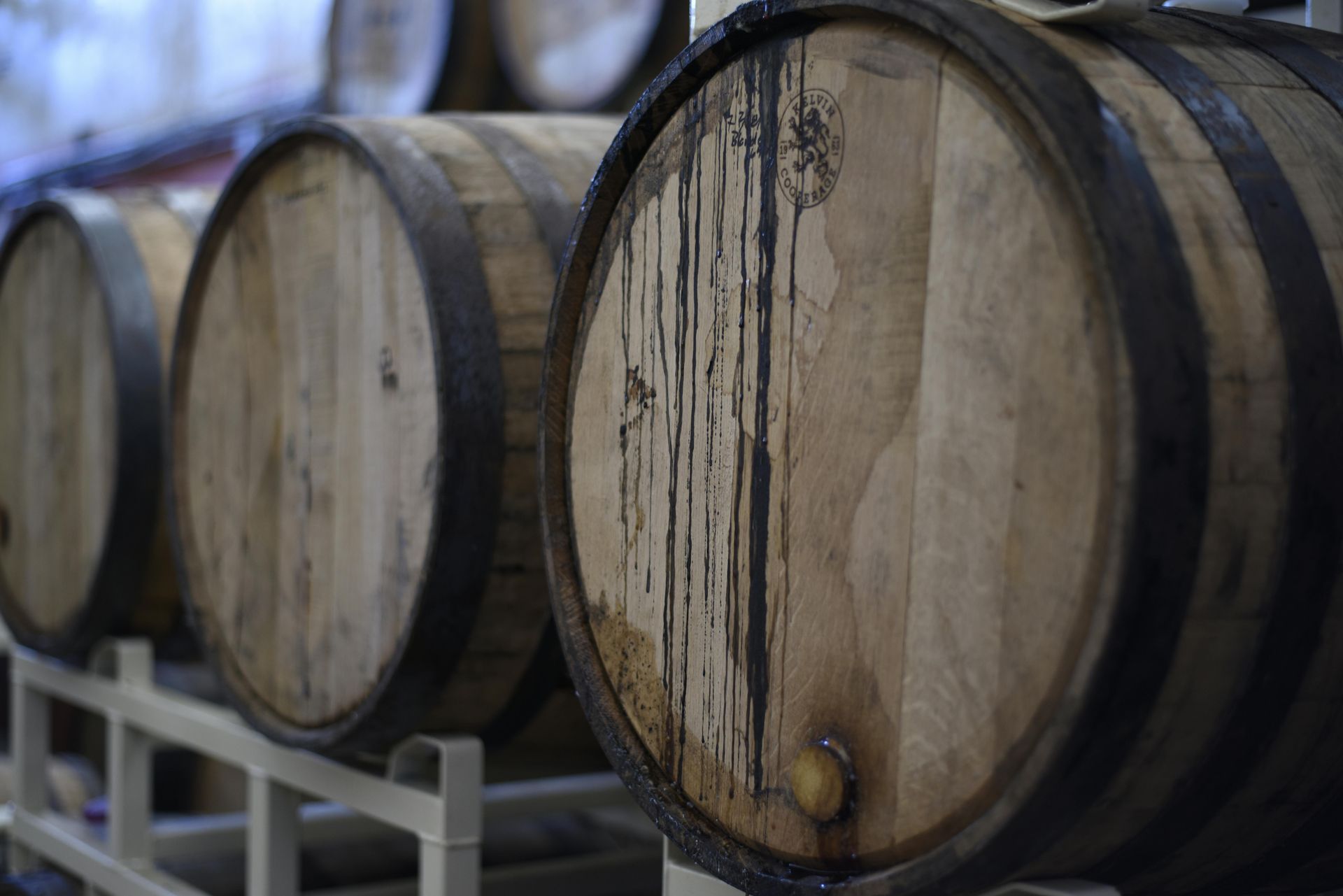Una fila de barriles de madera están alineados en un estante en una bodega.